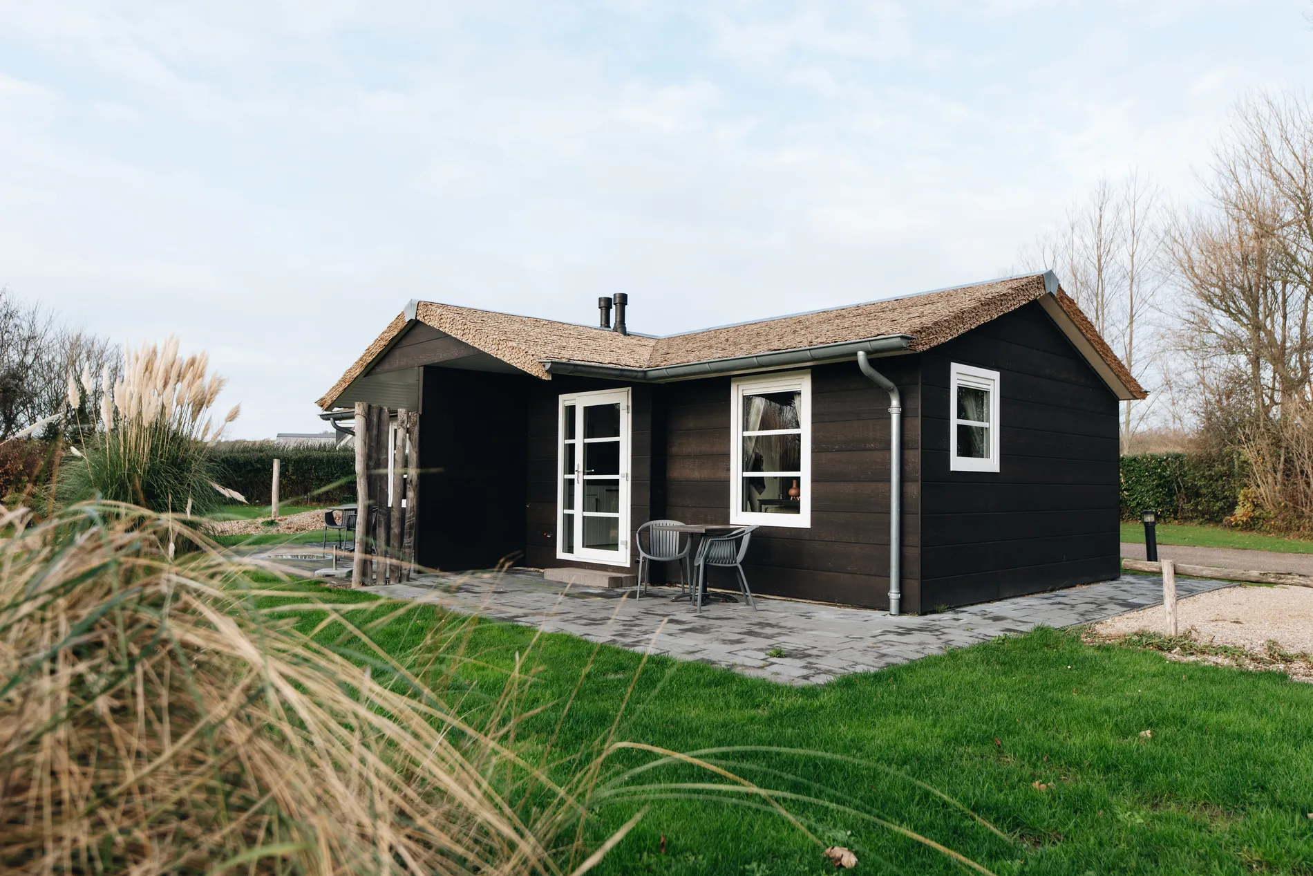 Moderne houten vakantielodge met rieten kap bij Resort Land & Zee, omgeven door natuur en voorzien van openslaande deuren naar het terras.